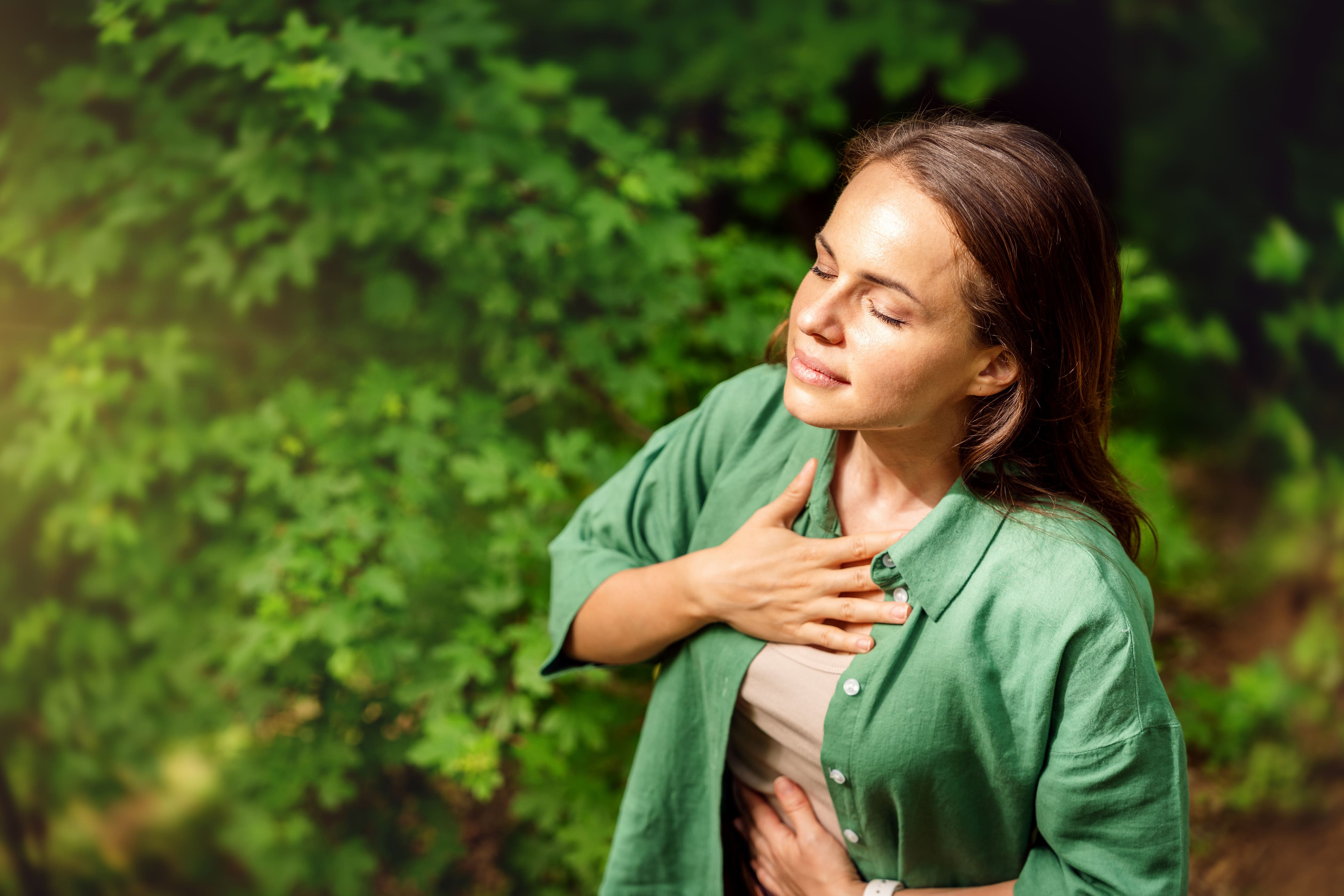 Frau ist draußen in der Natur und genießt diese mit einer Hand jeweils auf der Brust und dem Bauch